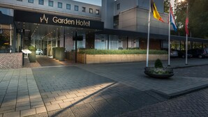 The exterior of the Garden Hotel with a modern design, featuring a glass facade, a brick entrance, and a landscaped area with a planter. - Bilderberg Garden Hotel (Amsterdam)