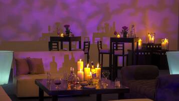 Un'area lounge scarsamente illuminata con un divano, un tavolino da caffè e un tavolo da pranzo apparecchiato con candele e bicchieri.
