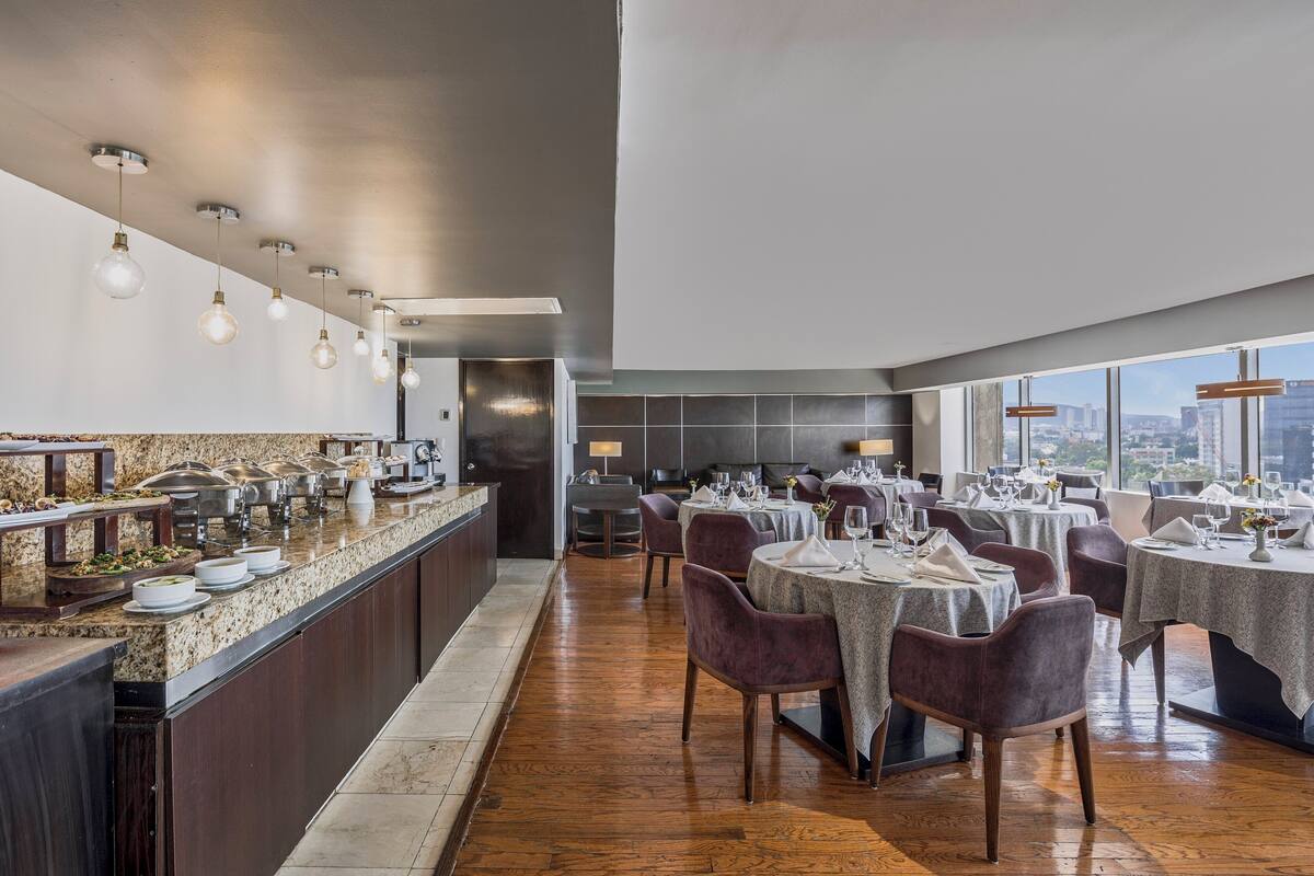 Een modern restaurant met een lange toonbank, meerdere eettafels en uitzicht op de stad.