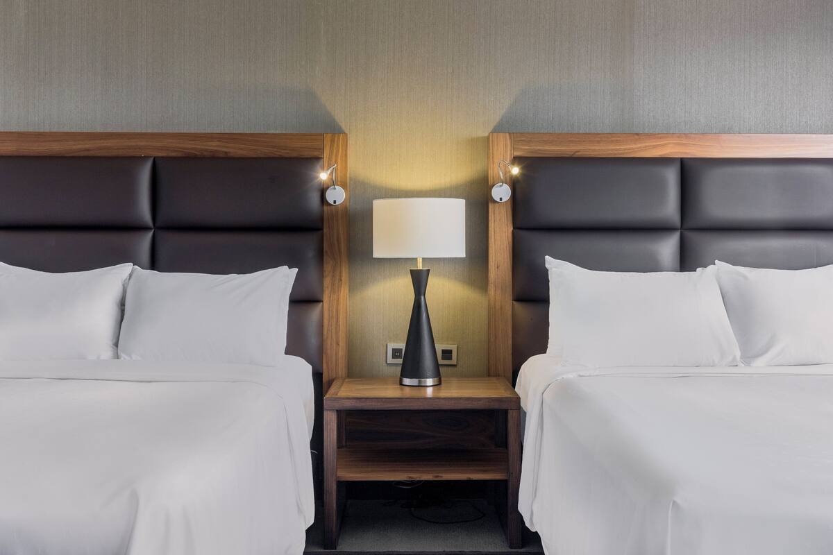 Een hotelkamer met twee bedden, een nachtkastje met een lamp en een houten hoofdbord.