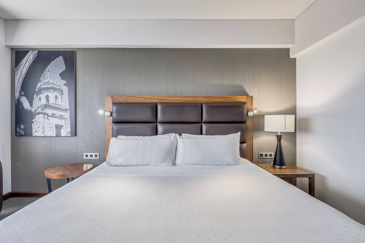 Een hotelkamer met een groot bed, een hoofdbord, twee nachtkastjes met lampen en een kunstwerk aan de muur.