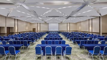 A conference room with rows of blue chairs and tables, a patterned carpet, and a modern ceiling design.