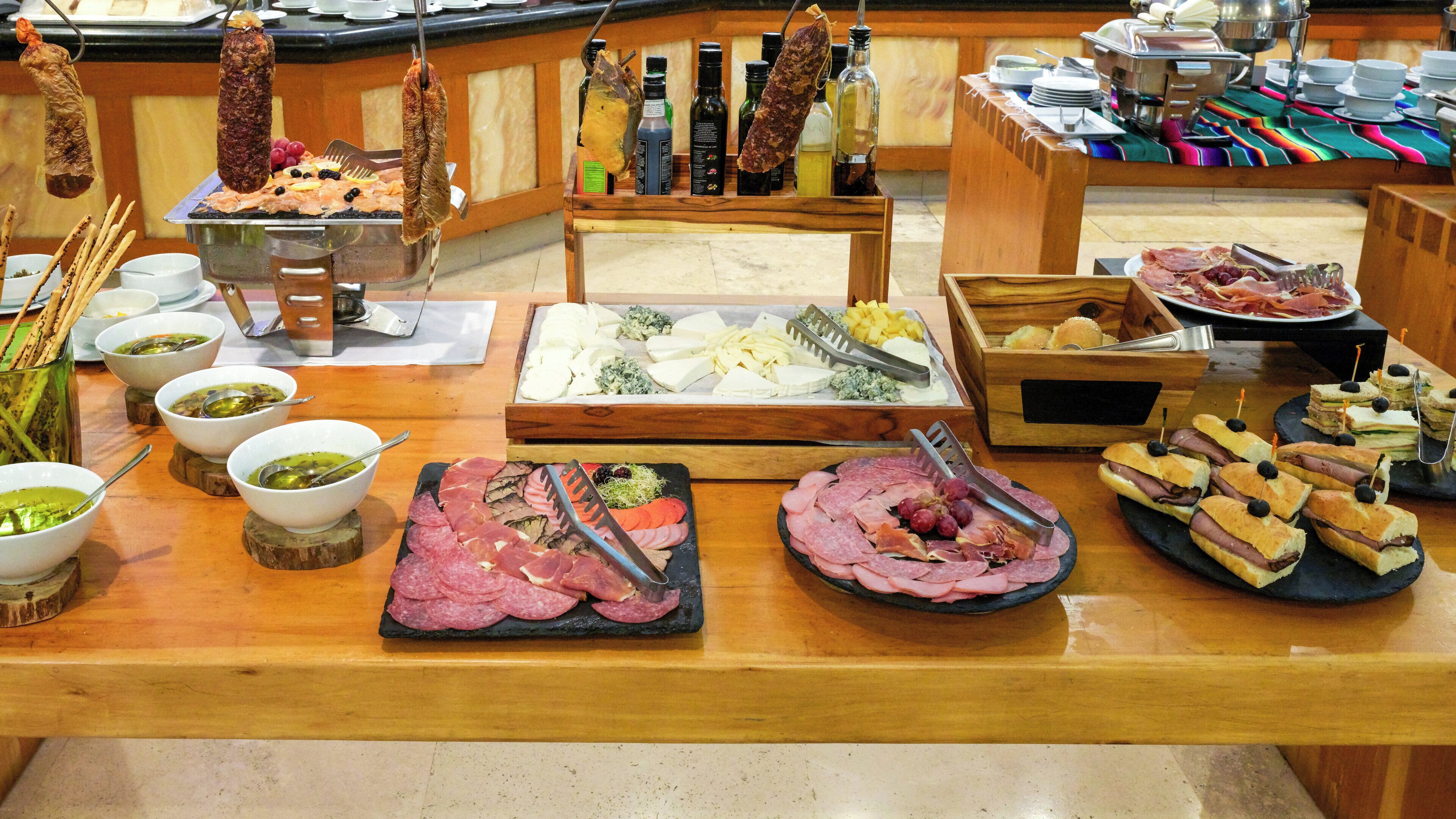 A buffet with various meats, cheeses, and breads.