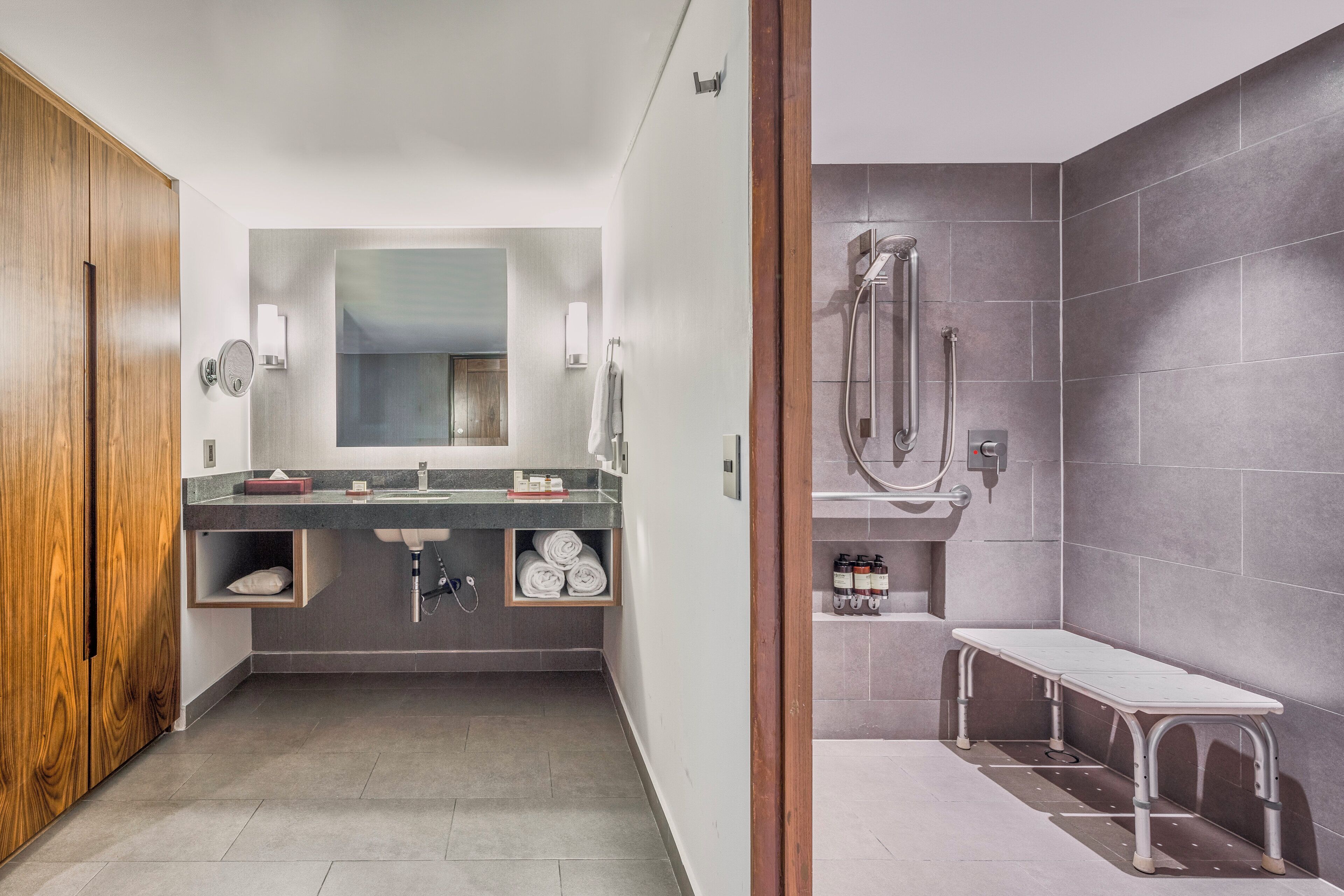 A modern bathroom with a wooden vanity, a large mirror, and a shower area with a bench.