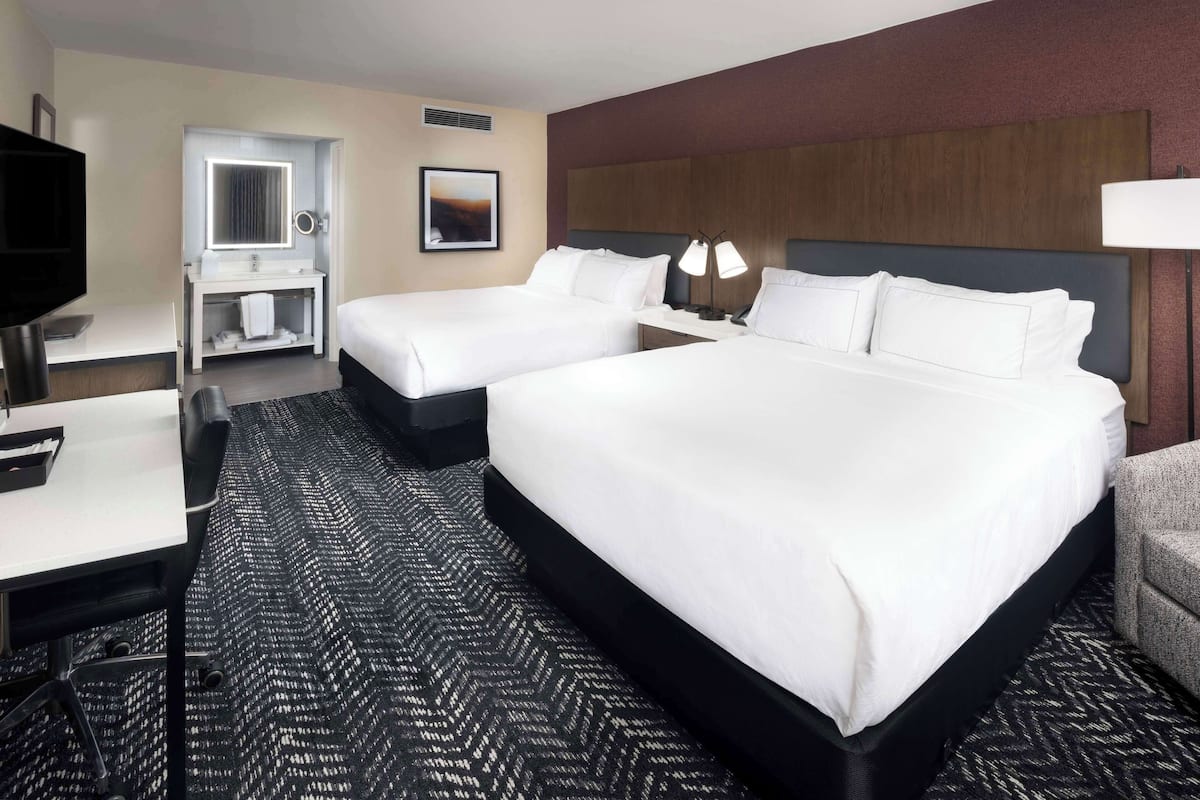 Habitación de hotel con dos camas, un escritorio, un tocador con espejo y un televisor.