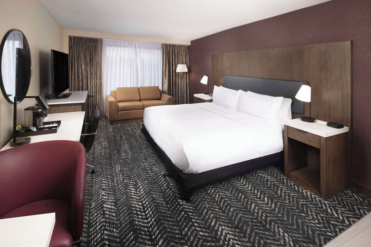 Habitación de hotel con una cama grande, un escritorio con computadora, televisor, sofá y espejo.