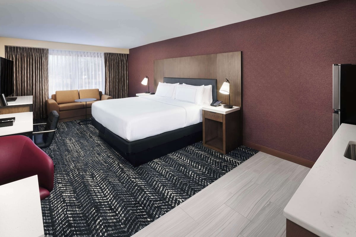 Habitación de hotel con una cama grande, un escritorio, una silla, un televisor y una ventana con cortinas.