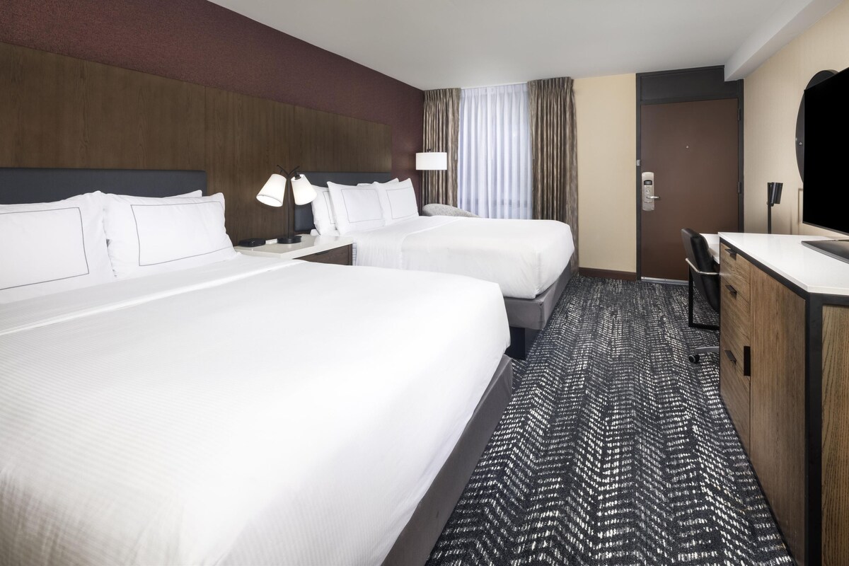 A hotel room with two beds, a desk, a chair, a TV, and a bathroom door.