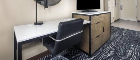 Una habitación de hotel con escritorio, silla, televisor y puerta.