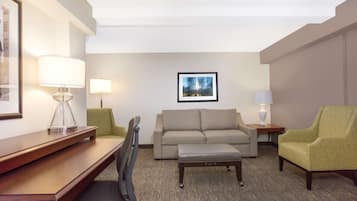 A hotel room with a wooden desk, two chairs, a sofa, a small table, and a lamp.