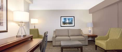 A hotel room with a wooden desk, two chairs, a sofa, a small table, and a lamp.