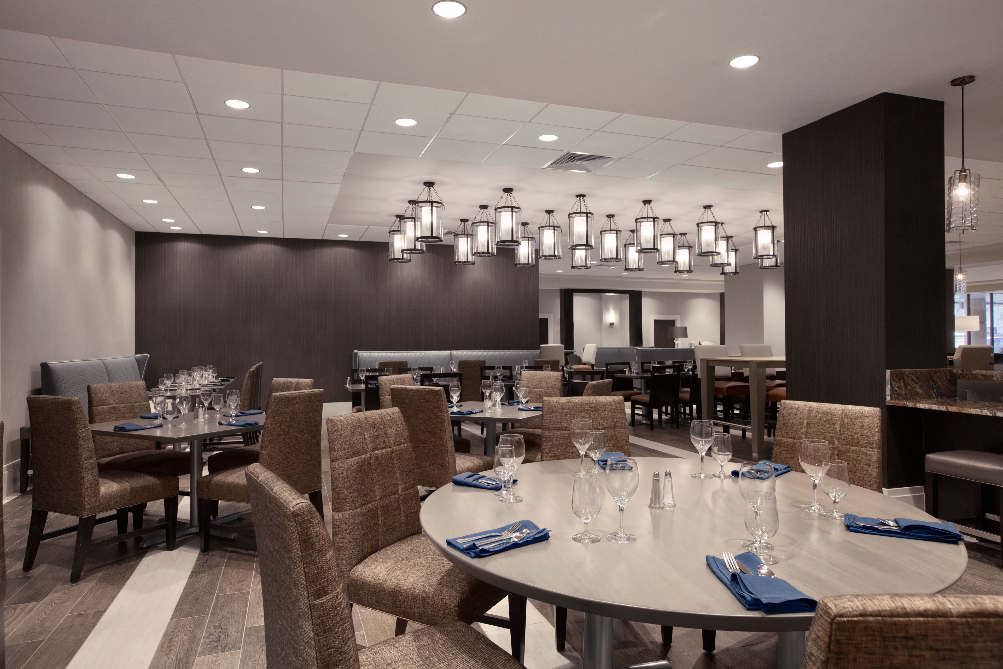 A modern dining area with round tables, brown upholstered chairs, and pendant lighting.