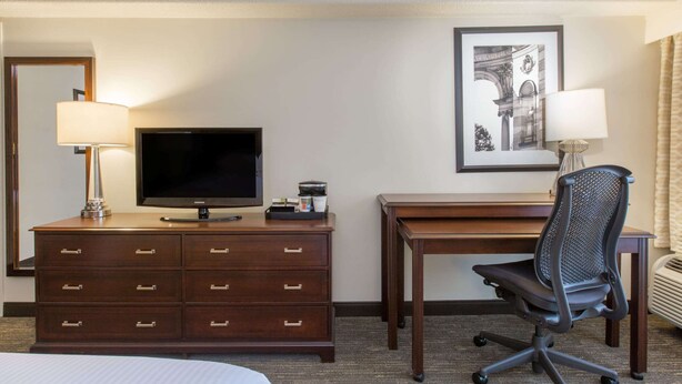 A hotel room with a bed, a TV on a wooden dresser, a desk with a chair, and a framed picture on the wall. - Wyndham Philadelphia Historic District (Philadelphia)
