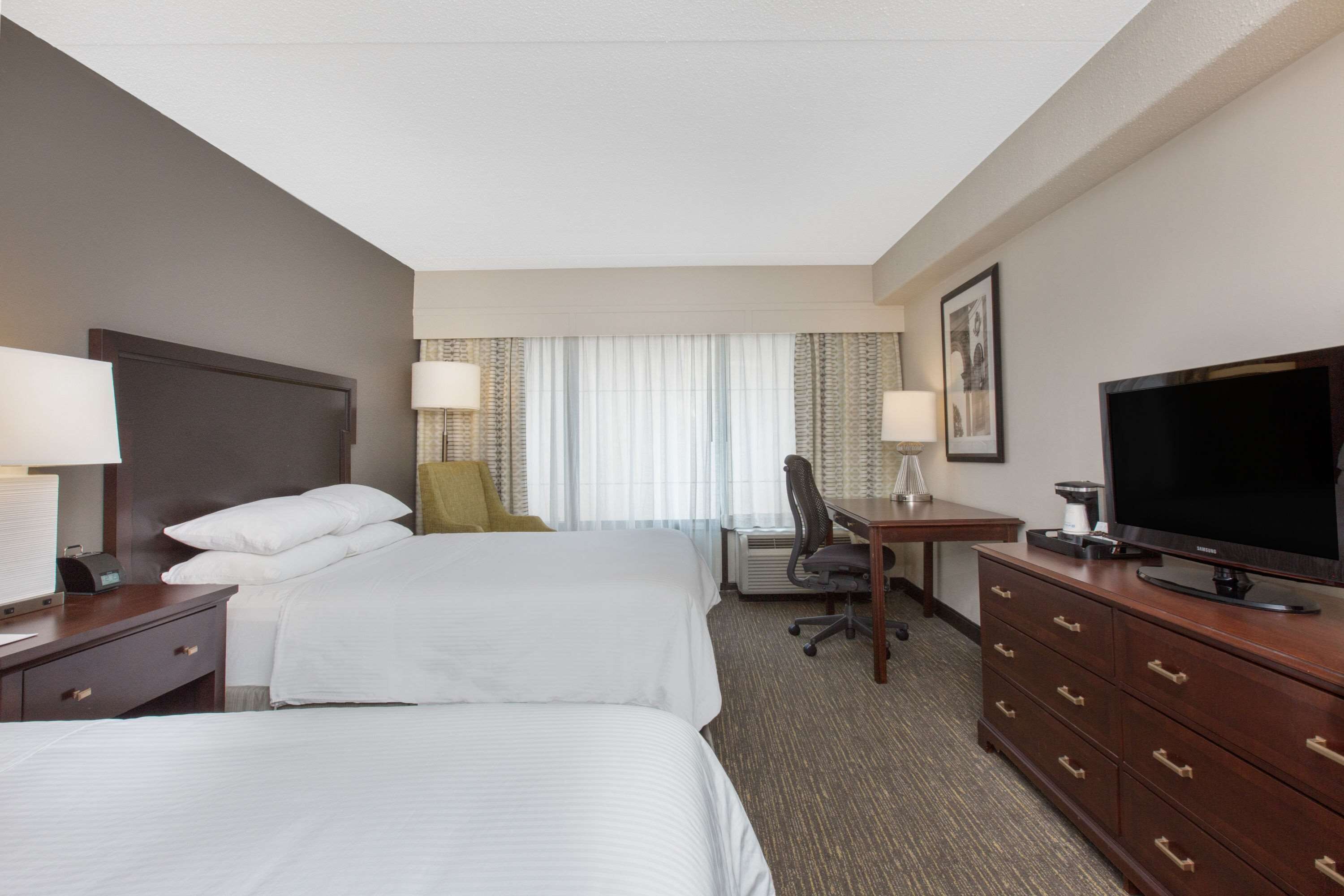 A hotel room with two beds, a desk, a television, and a chair.