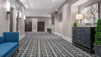 Un hall d’hôtel avec un tapis à motifs, un canapé bleu, un buffet en bois foncé et une lampe fixée au mur.