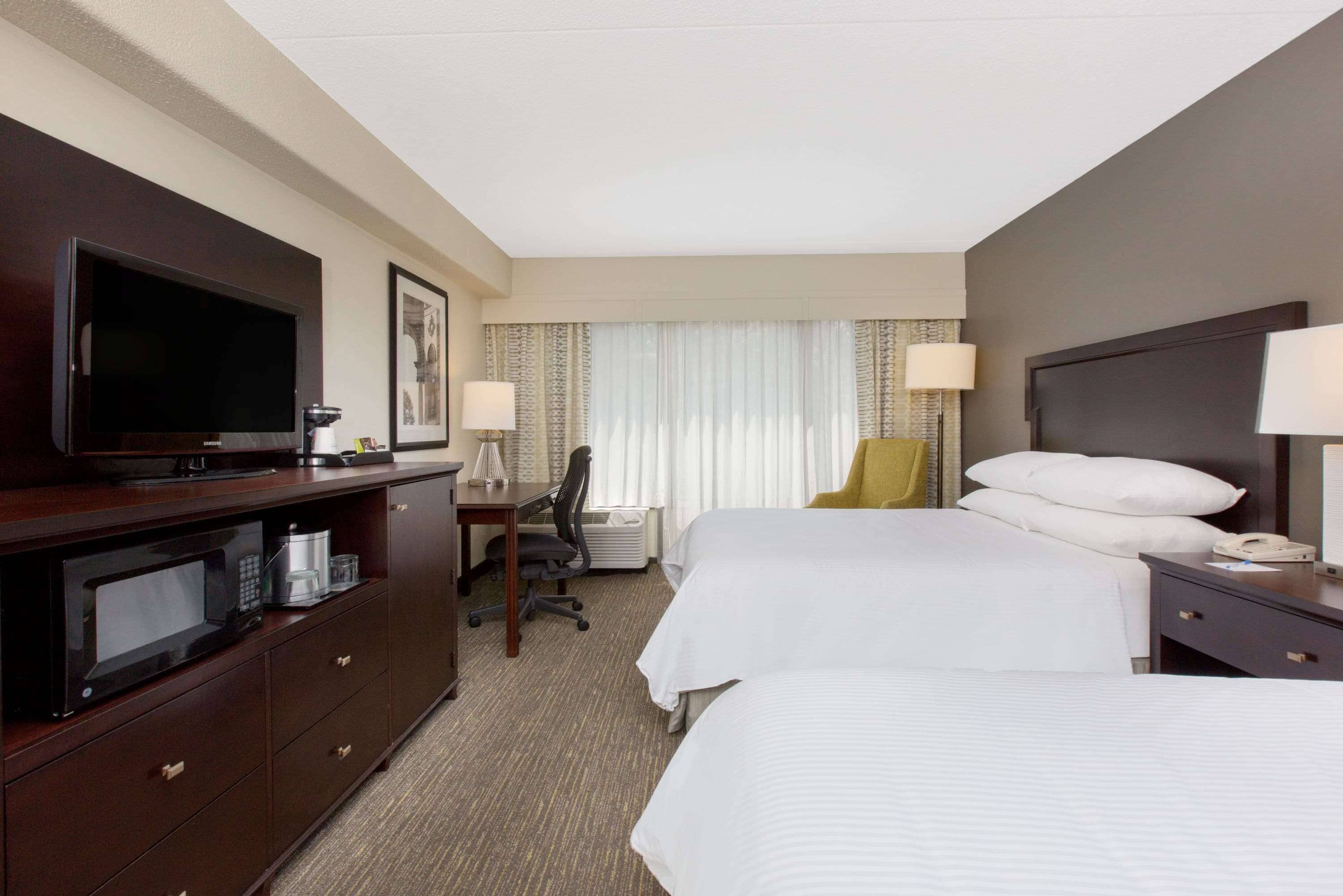 A hotel room with two beds, a desk, a television, and a minibar.