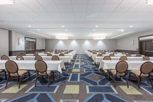Un salón de conferencias con mesas y sillas dispuestas en filas, alfombra estampada e iluminación empotrada.