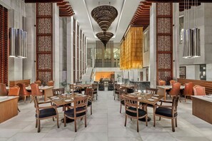 A spacious dining area with multiple tables and chairs, a central staircase, and decorative wooden panels. - ITC Mughal, A Luxury Collection Resort & Spa, Agra (Agra)