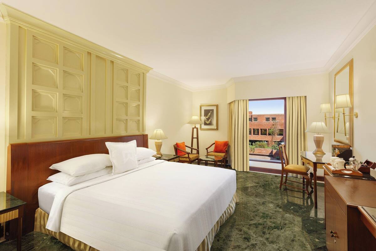 A hotel room with a large bed, a desk, a chair, and a view of the outside.