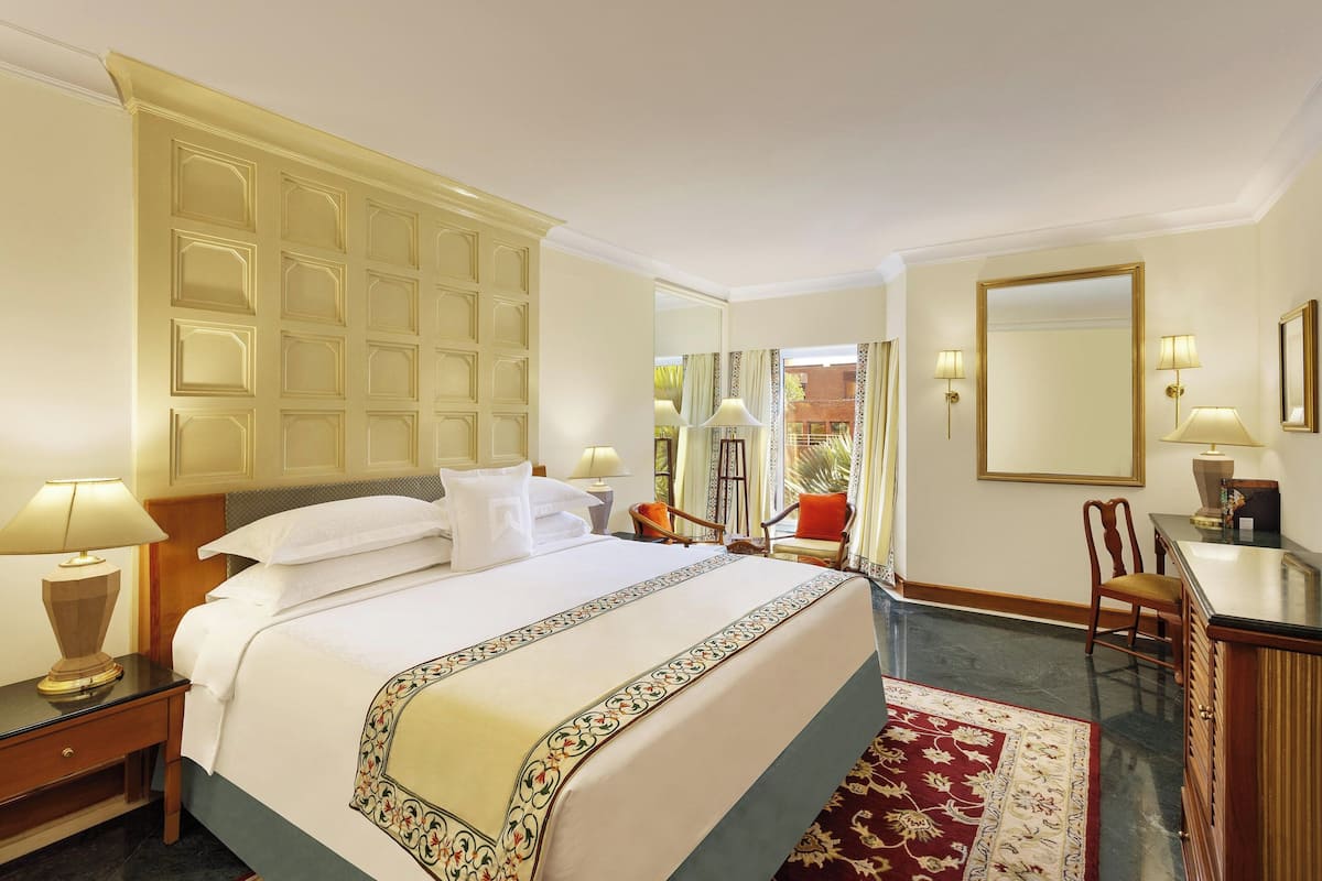 A hotel room with a large bed, a desk with a chair, a mirror, and a view of the outside.