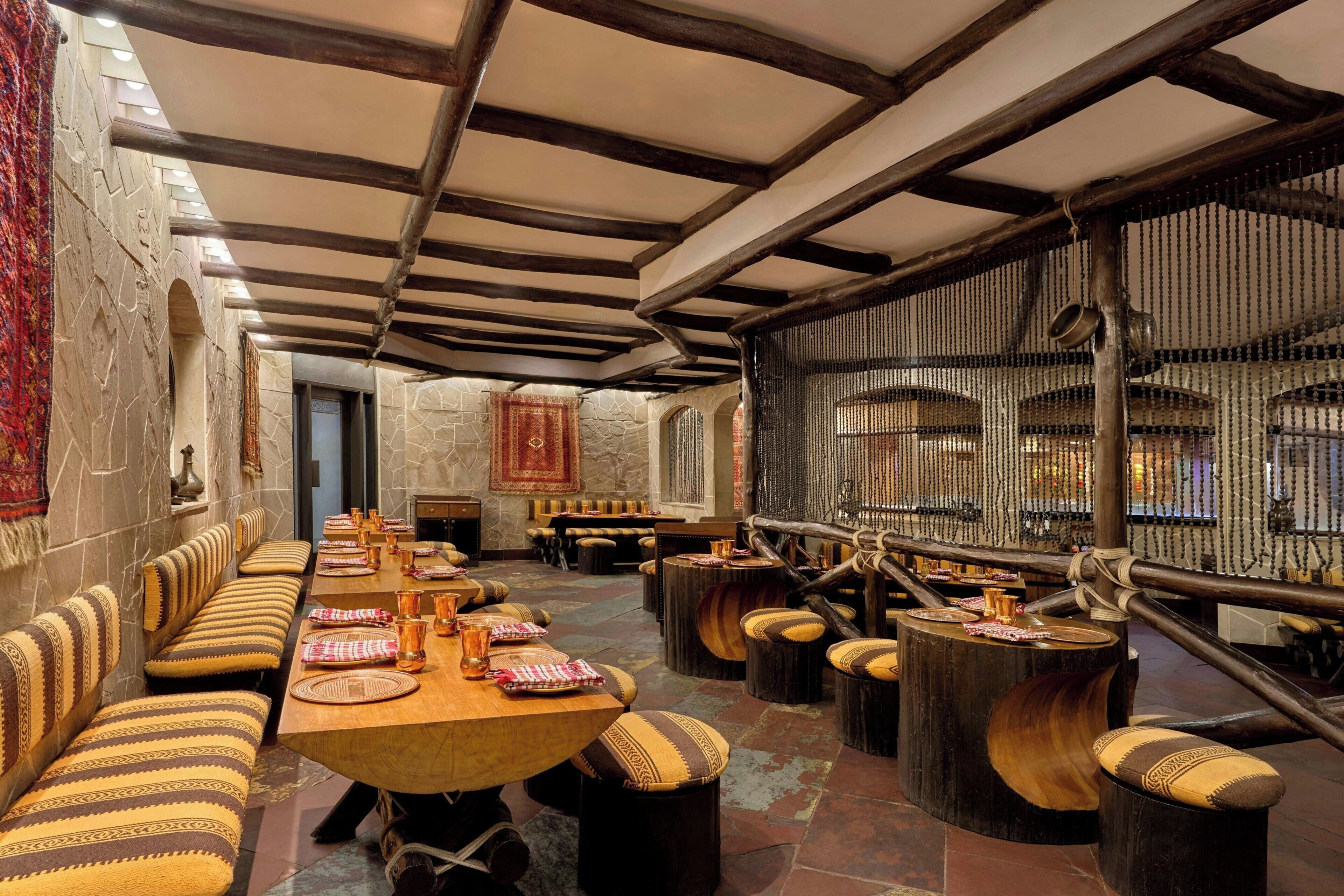 Una larga mesa de comedor con múltiples sillas, una pared de piedra y una estructura de techo de madera.