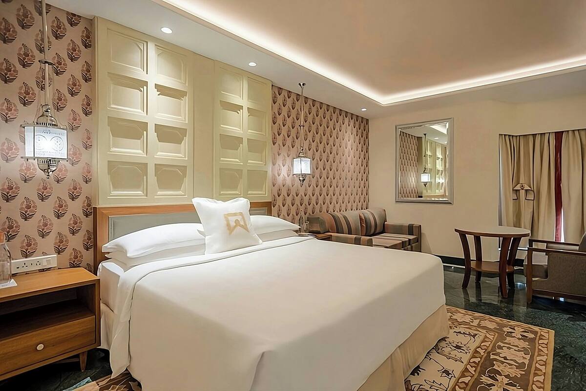 A hotel room with a large bed, a sofa, a small table, and a mirror.