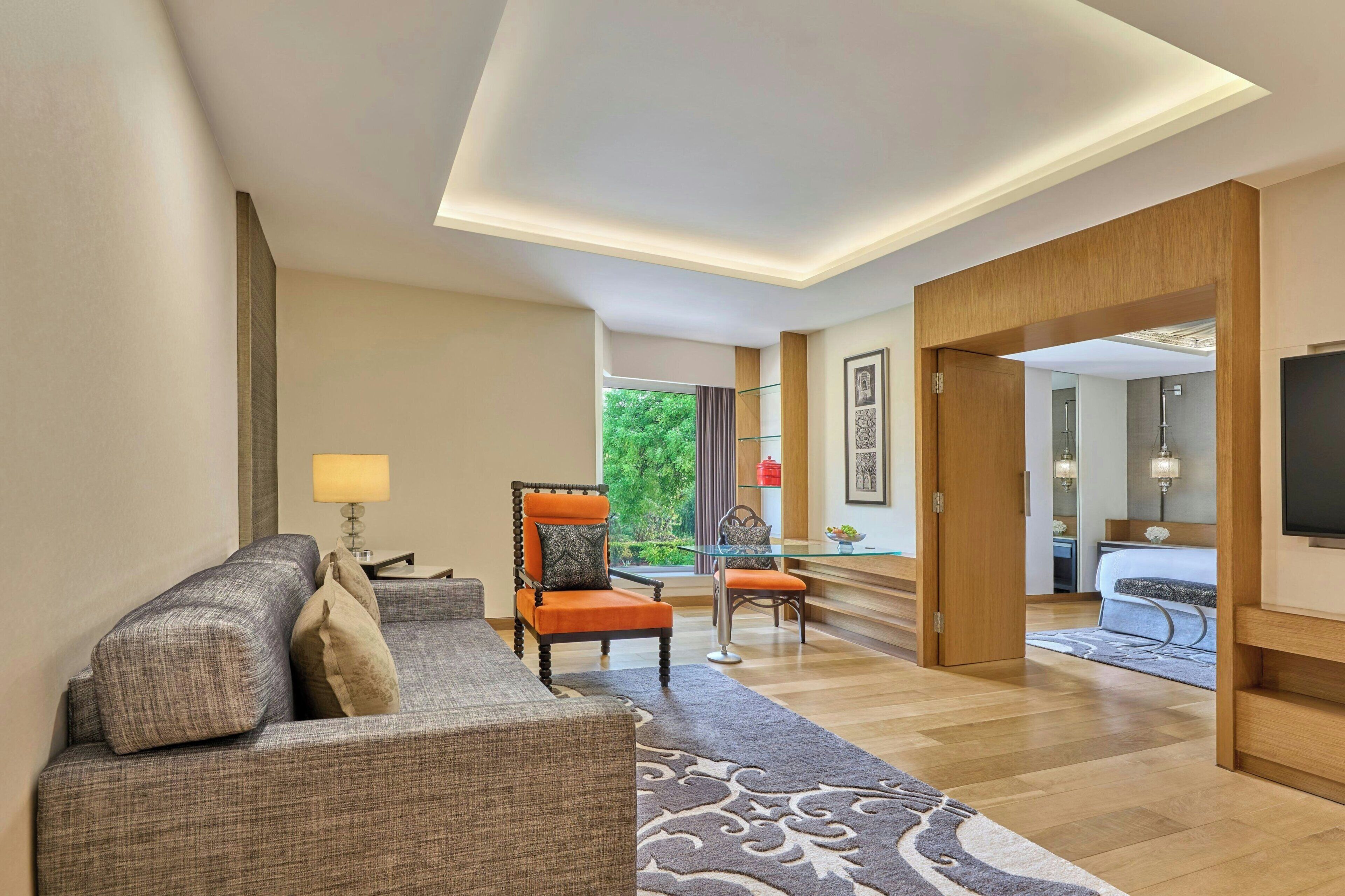 Uma sala de estar moderna com um sofá, poltrona e mesa de centro de vidro. Vê-se um jardim através de uma janela.