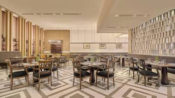 A spacious dining area with multiple tables and chairs, a patterned floor, and a decorative wall with framed artwork.