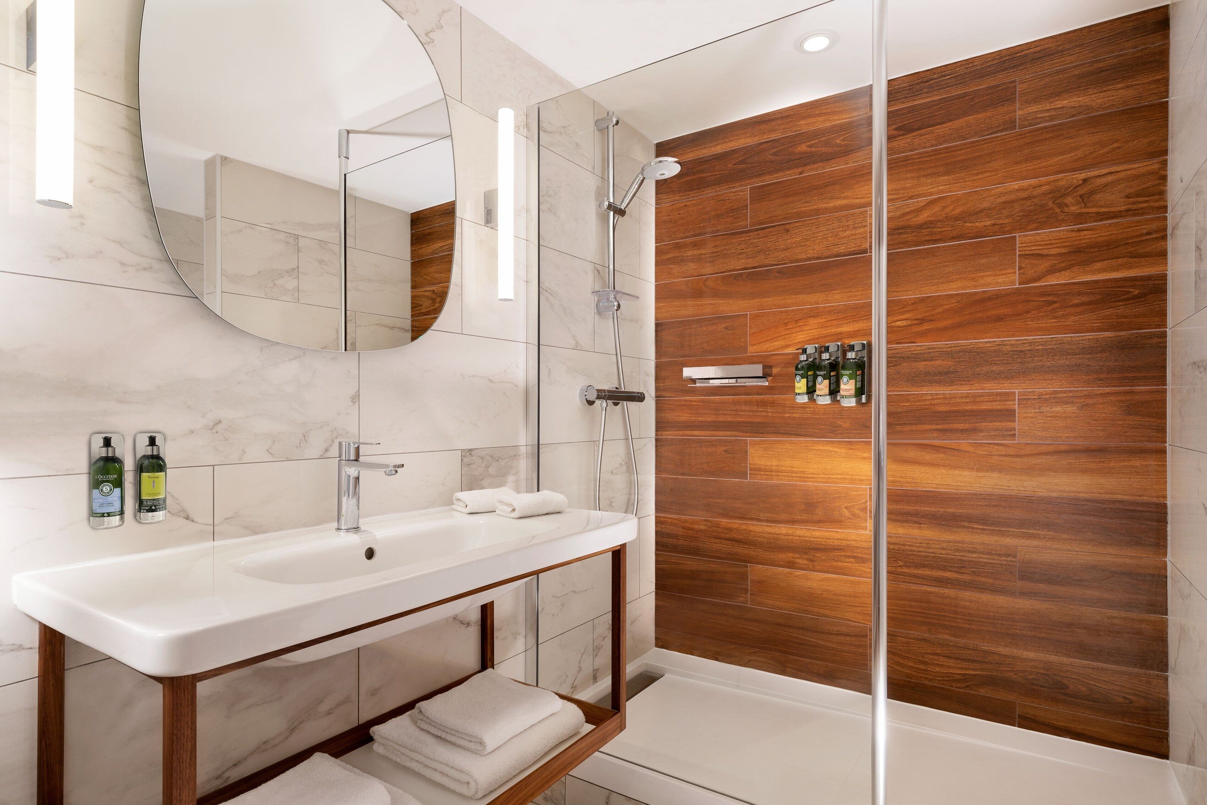 Een moderne badkamer met een marmeren wastafel, houten lambrisering en een douchecabine met glazen wanden.