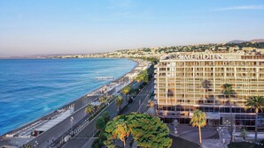 Un hotel frente al mar, con vista al océano, un paseo marítimo y un edificio grande con balcones.