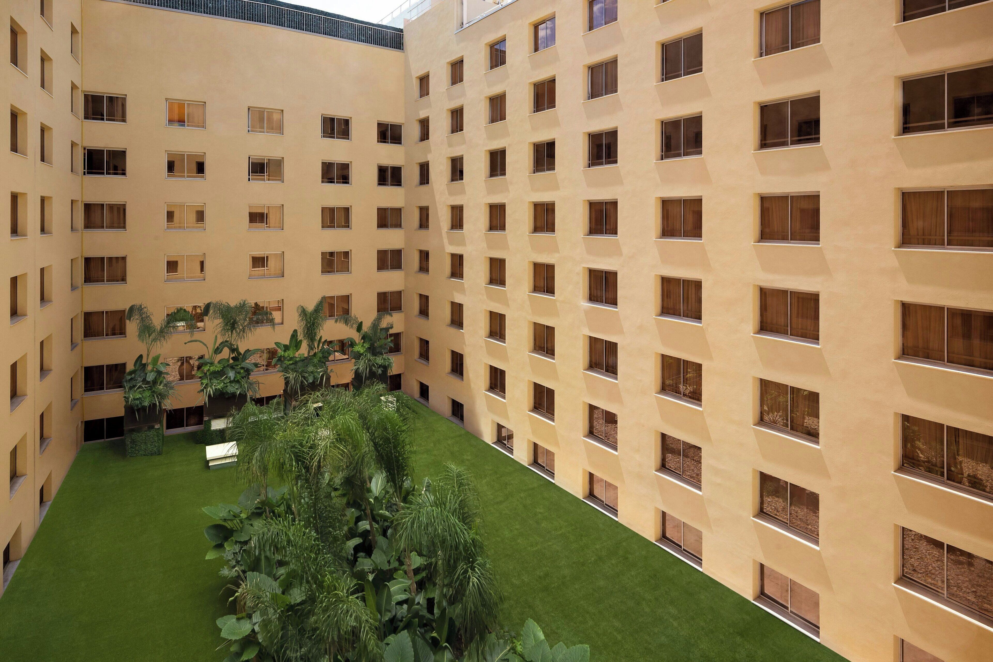 A multi-story hotel with a central courtyard featuring green grass and potted plants.