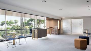 Un espacio de oficina moderno con un ventanal grande, una mesa redonda con sillas y una pequeña zona de estar con un sofá y reposapiés.