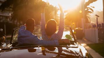 Un'auto decappottabile con due persone, una delle quali alza la mano.