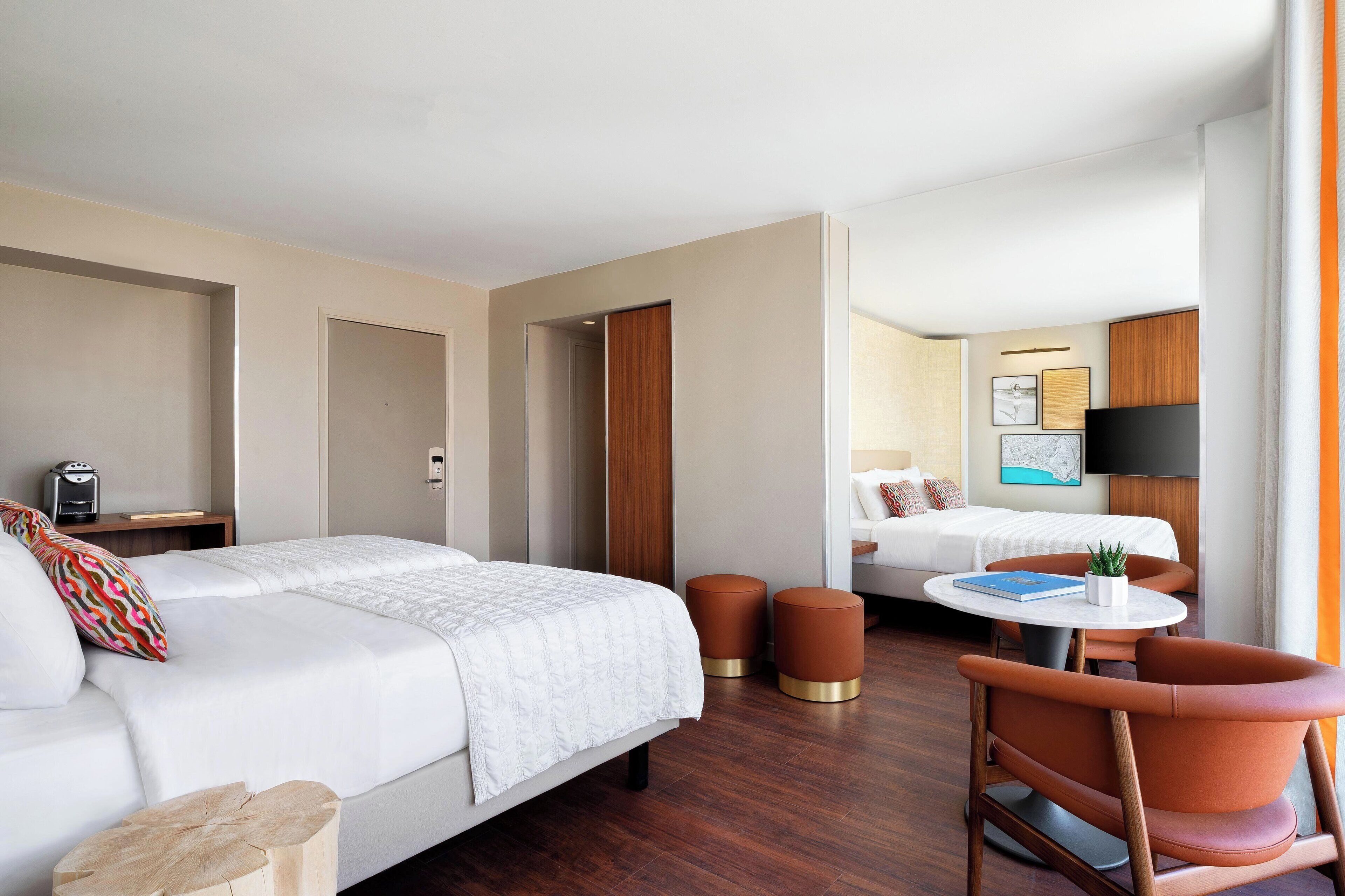 Habitación de hotel con cama, escritorio con silla, mesita con planta y televisor.
