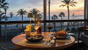 Una mesa con comida, una copa de vino y vistas a palmeras y al océano.