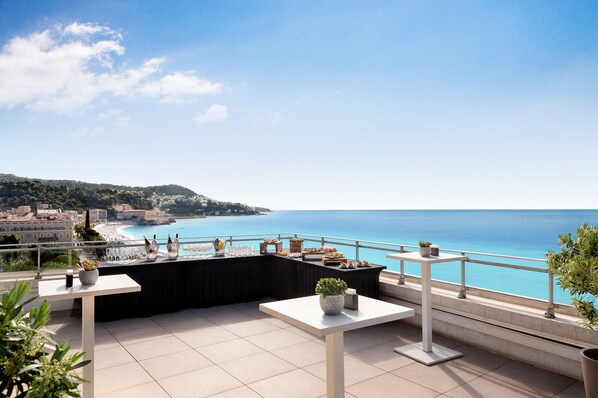 Una terraza con vista al mar, una disposición tipo bufé y plantas en macetas.