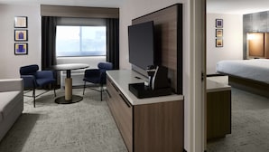 A hotel room with a bed, a desk with a TV, a seating area with chairs, and a large window. - Hampton Inn Newark Airport (Newark)