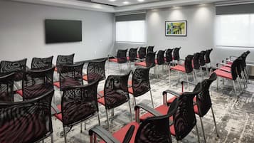 Un salón de conferencias con hileras de sillas, un televisor de pantalla plana grande y ventanas con persianas.