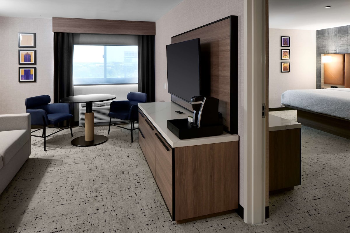 Ein Hotelzimmer mit Bett, Schreibtisch mit Flachbildfernseher, einer Sitzecke mit Stühlen und einem großen Fenster.