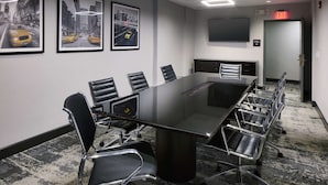 A conference room with a long table, black chairs, framed cityscape pictures, a flat-screen TV, and an exit sign. - Hampton Inn Newark Airport (Newark)