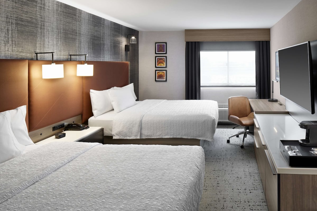 Ein Hotelzimmer mit zwei Betten, einem Schreibtisch, einem Stuhl, einem Fernseher und einem Fenster mit Vorhängen.