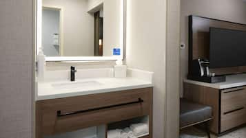 A modern bathroom with a large mirror, two sinks, a vanity with a towel rack, and a flat-screen TV on a wooden cabinet.
