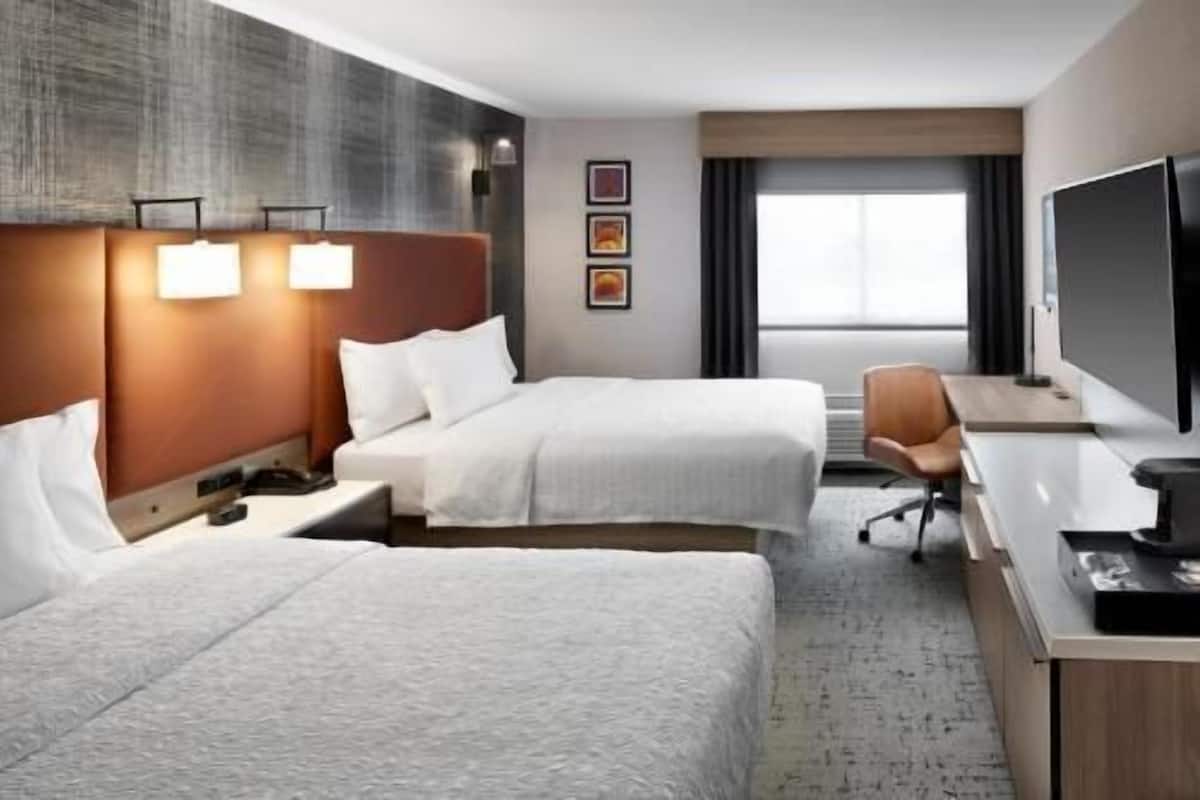 Ein Hotelzimmer mit zwei Betten, einem Schreibtisch, einem Stuhl, einem Fernseher und einem Fenster mit Vorhängen.