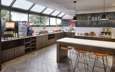 A modern kitchen with a bar area, herringbone-patterned flooring, and a large window providing natural light.