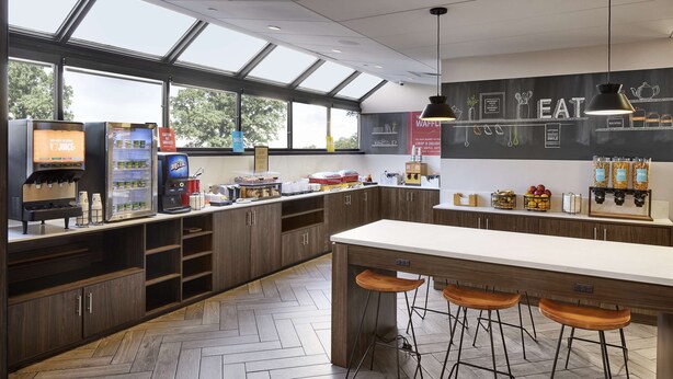 A modern kitchen with a bar area, herringbone-patterned flooring, and a large window providing natural light. - Hampton Inn Newark Airport (Newark)