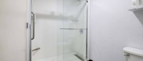A glass-enclosed shower with a white toilet and a towel rack.
