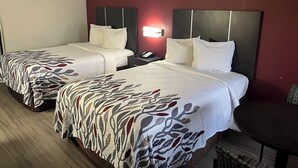 A hotel room with two beds, a nightstand with a phone, a wall-mounted light, and a small table. - Red Roof Inn Rockingham (Rockingham)