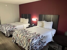 Habitación de hotel con dos camas, una mesita de noche con teléfono, una lámpara de pared y una pequeña mesa.