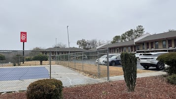 Ein durch Zäune abgegrenzter Parkbereich mit einem Red Roof Inn Schild, ein Gebäude mit rotem Dach und einem wolkenlosen Himmel.