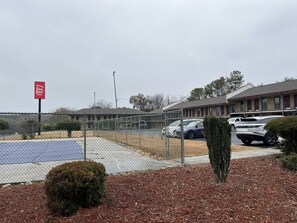 Un'area di parcheggio recintata con il cartello Red Roof Inn, un edificio con tetto rosso e cielo sereno.